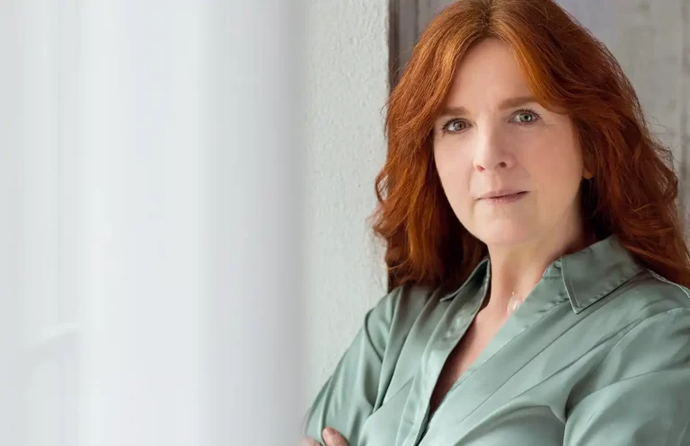Isabel Walter mit langen roten Haaren und grüner Bluse blickt direkt in die Kamera vor hellem Hintergrund.